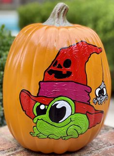 a painted pumpkin with a frog wearing a witch's hat on it sitting on a rock