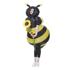 a woman in a bee costume holding sunflowers while standing next to a giant balloon