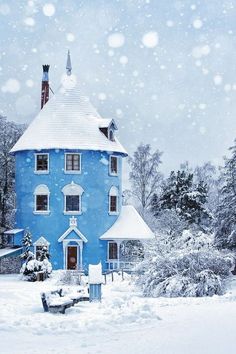 a blue house is covered in snow and surrounded by trees