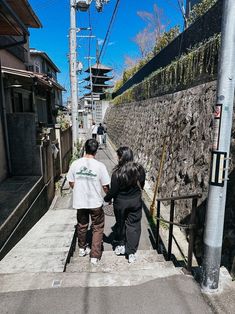 two people sitting on the side of a road next to a stone wall and power lines