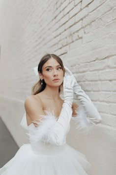 a woman in a white dress leaning against a brick wall