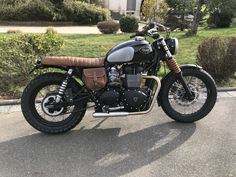 a black motorcycle parked on the street in front of some bushes and trees with grass behind it