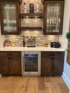 a kitchen with wooden cabinets and white counter tops, wine glasses on the glass shelves