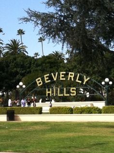 the beverly hills sign is in front of some trees and people are walking by it