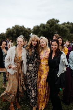 three women standing next to each other in front of a group of people at an outdoor event