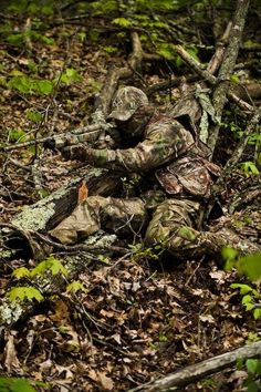 a camouflaged soldier laying on the ground in the woods