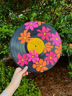 a hand holding an old record with flowers painted on it and pointing to the side