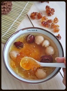 a person holding a spoon over a bowl of soup with nuts and raisins