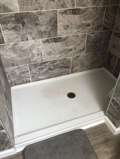 a shower stall with a gray rug on the floor and grey tile wall behind it