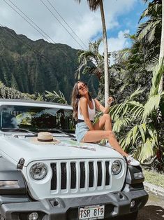 a woman sitting on the hood of a white jeep parked in front of palm trees