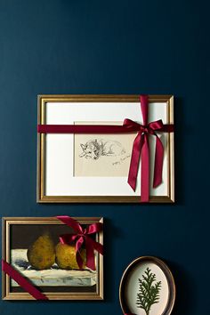 two framed pictures hang on the wall next to each other with red ribbons tied around them