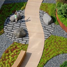 a small child is standing on a wooden walkway between two large rocks and green grass