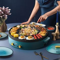 a woman preparing food on top of a blue table with plates and utensils