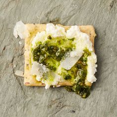 a piece of food that is sitting on some kind of stone slab with cheese and pesto