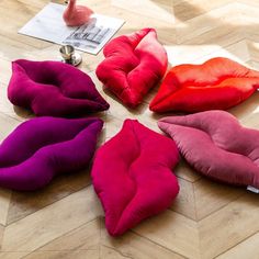 six different colored pillows laid out on a wooden floor next to a small pink bird