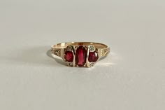 This is a gorgeous Edwardian Era 14k Yellow Gold Garnet Ring with a three genuine garnets and four white sapphire gemstone setting, the middle garnet is oval faceted cut the two side ones are faceted round cut, with four rose cut white sapphires one on each corner. A stunning piece of fine early 1900s era jewelry, featuring January's birthstone! ERA - Circa 1900s / Edwardian METAL / MATERIAL - 14k yellow gold, 3 genuine garnets (approx. 0.77 CTW), 4 white sapphires (approx. 0.02 CTW) MARKINGS / Gold And Garnet Jewelry, Heirloom Ruby Three-stone Ring, Heirloom Ruby Ring With Three Stones, Heirloom Ruby Three Stone Ring, Heirloom Three Stone Red Rings, Antique Three Stone 14k Gold Jewelry, Heirloom Three-stone Sapphire Ring In 14k Gold, Victorian 14k Gold Three-stone Ring, Victorian Three Stone 14k Gold Ring