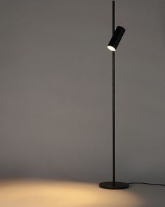 a black floor lamp with a white light on it's side and a gray wall in the background