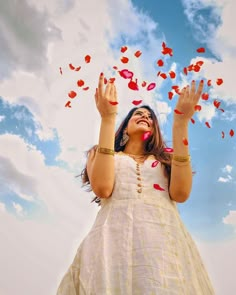 a woman in a white dress is throwing petals into the air with her hands and eyes wide open