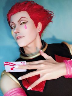 a woman with red hair and pink nails holding a white object in her hand while wearing a black shirt