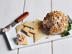 a white plate topped with crackers and cheese covered in nuts next to a knife