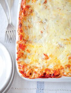 a casserole dish with meat and cheese on it next to a plate, fork and knife