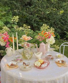 a table that has some tea cups and saucers on it with flowers in the background