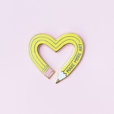 a yellow heart shaped pin with a pencil in it's center on a pink background