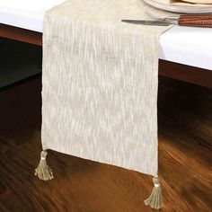 a white table runner with tassels and a plate on the side next to it