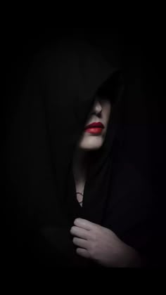 a woman with red lips and black hoodie in the dark holding her hands on her chest