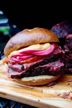 a roast beef sandwich with red onions and mustard on a wooden cutting board next to a bbq