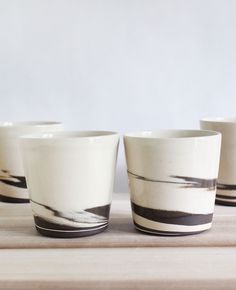 four white cups sitting on top of a wooden table next to each other with black and white designs