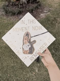 someone holding up a graduation cap that says in this moment now