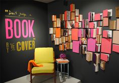 a yellow chair sitting in front of a black wall with books on it and a sign that reads book by the cover