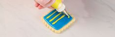 someone is decorating a cookie with yellow icing on it while holding a toothbrush in their hand