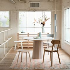 a white table with four chairs and a vase on top of it in front of some windows