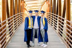 three men in graduation gowns are standing on a wooden bridge and posing for the camera