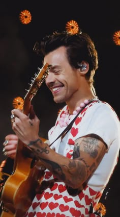 a man with tattoos holding a guitar in his hand and smiling at the camera while standing on stage