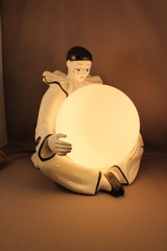 a white statue holding a round light in it's hands and sitting on the ground