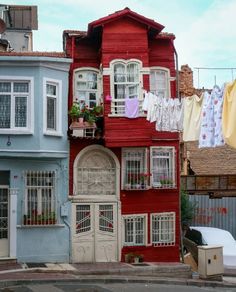 a red house with white windows and balconies on the roof is next to other buildings