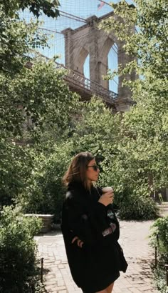 a woman standing in front of the brooklyn bridge with her hands on her hips while holding a cup of coffee