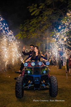 two people riding on the back of a four - wheeler with lights in the background