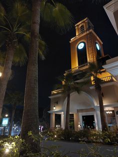 a clock tower is lit up at night in front of some palm trees and buildings