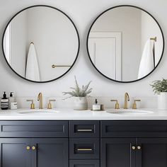 two round mirrors hanging on the wall above double sinks in a white and black bathroom