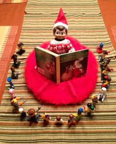 an elf reading a book on top of a table with small figurines around it