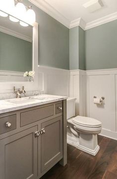 a white toilet sitting under a bathroom mirror next to a sink and a wooden floor