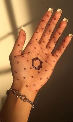 a woman's hand with tattoos on it and a chain around the wrist that has hearts all over it