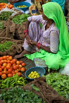 a woman sitting on the ground surrounded by vegetables