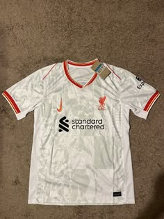 the shirt is white with orange trims and has a liverpool logo on it,