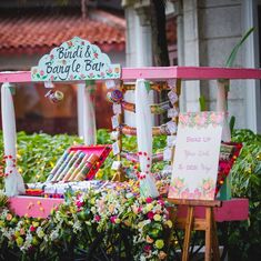 a sign that is sitting in front of some plants and flowers on the side of a building