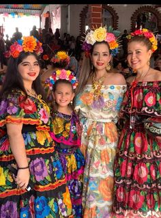 three women in colorful dresses standing next to each other with flowers on their head and arms